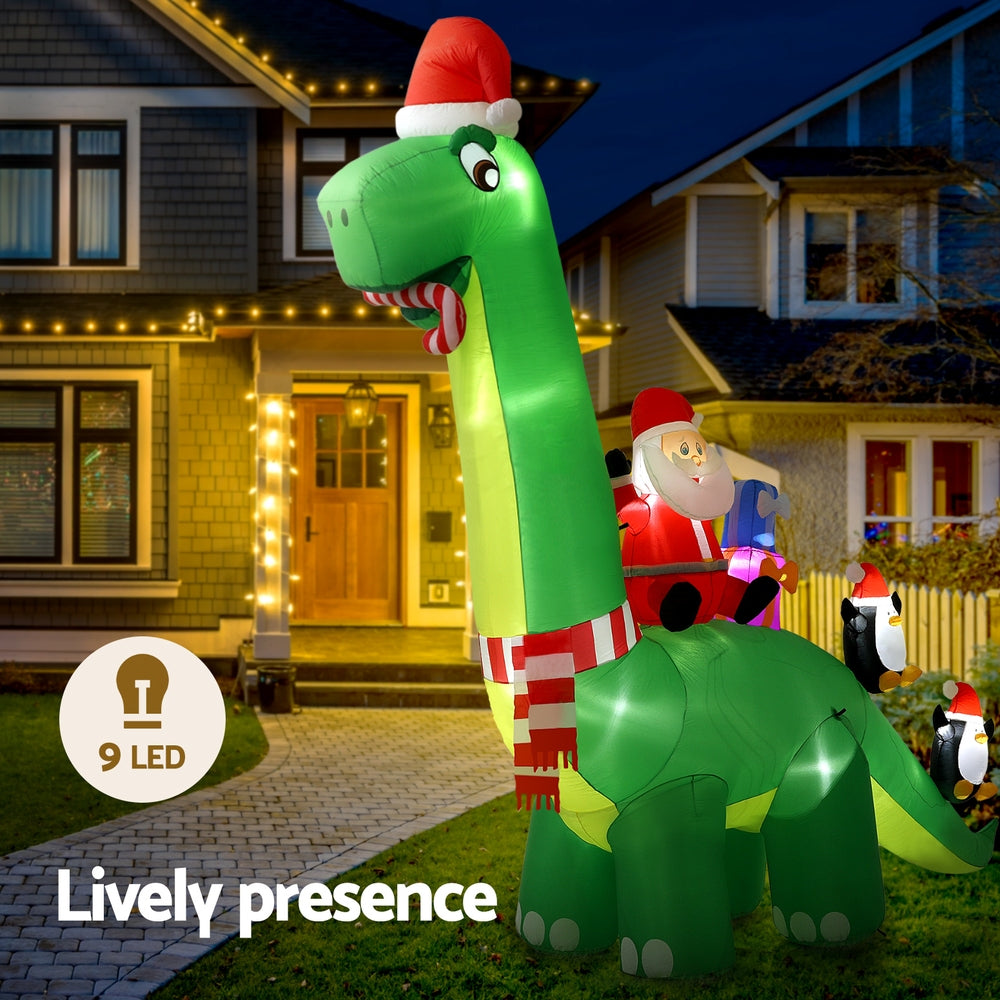 Illuminated green inflatable Santa riding dinosaur with penguin lights in yard