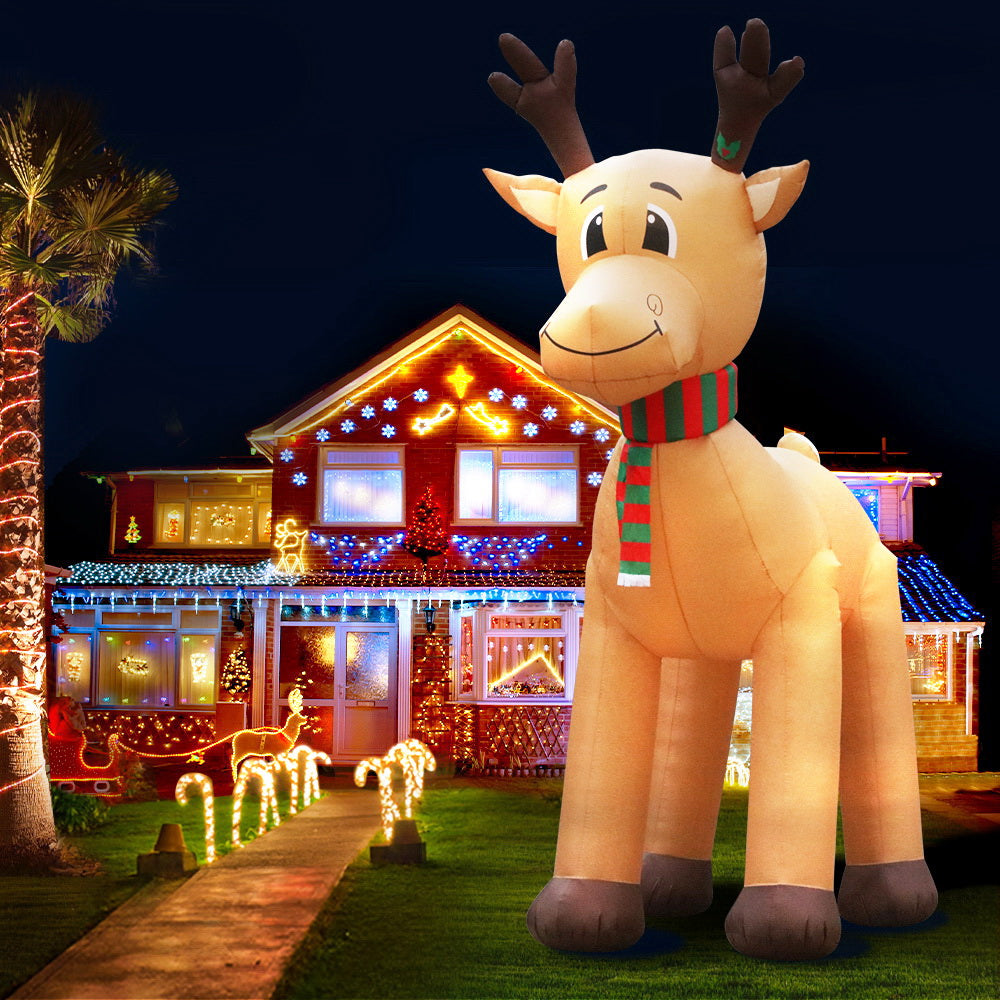 Illuminated inflatable reindeer decoration standing on lawn, striped scarf, tan body and hooves