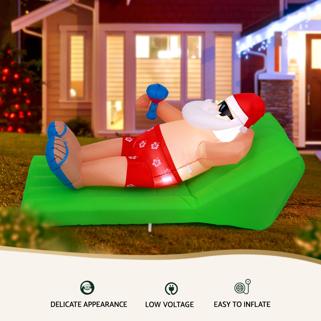 Inflatable Santa bench with Santa in red suit, white hat and beard, blue boots on green cushion.