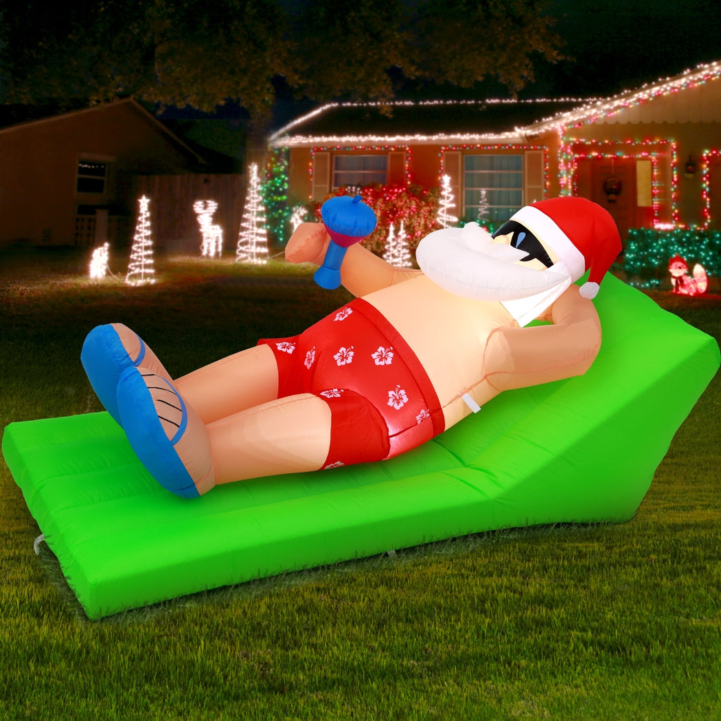 Inflatable Santa bench with Santa in red suit, white hat and beard, blue boots on green cushion.