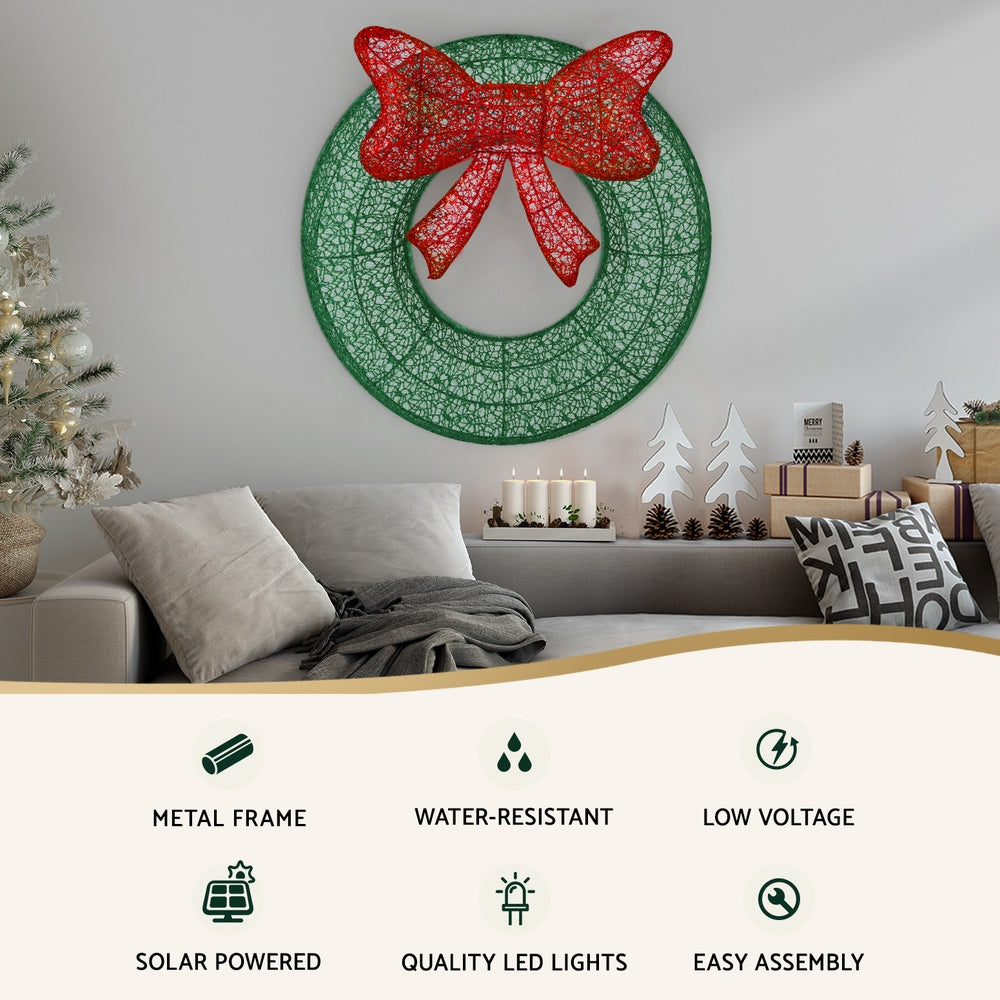 Solar wreath light decoration with red bow on green circular mesh, emitting green LEDs