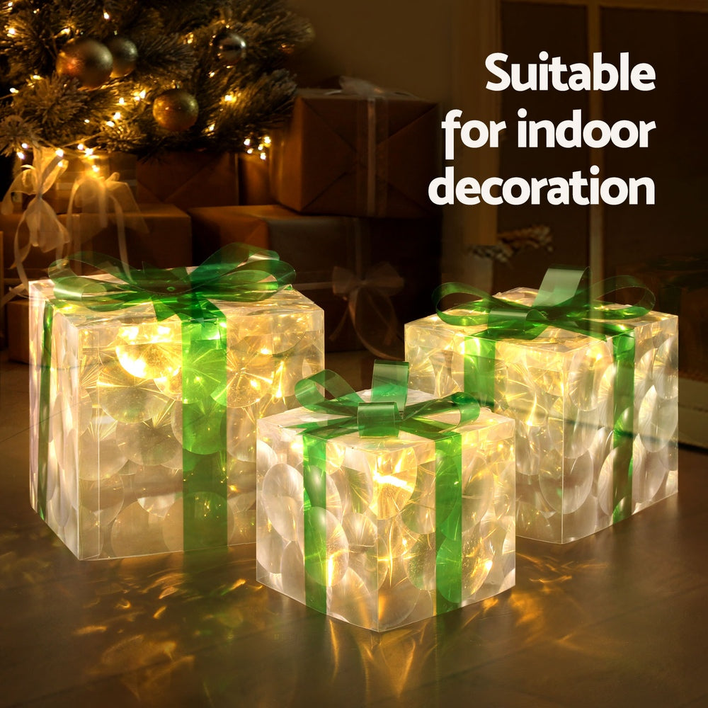 Set of 3 warm-glowing gift-box fairy lights with green bows in dark scene.