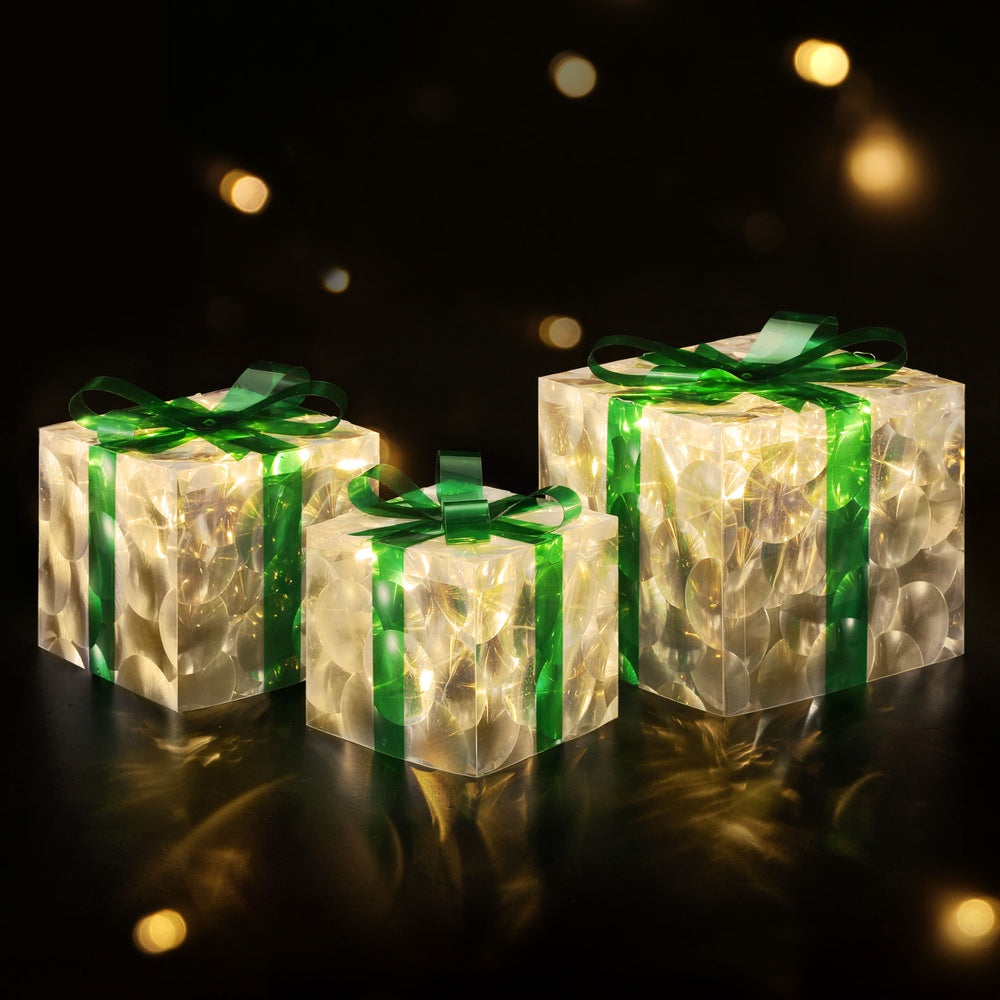 Three warm-lit gift-box fairy lights with green ribbons, glowing in dark.