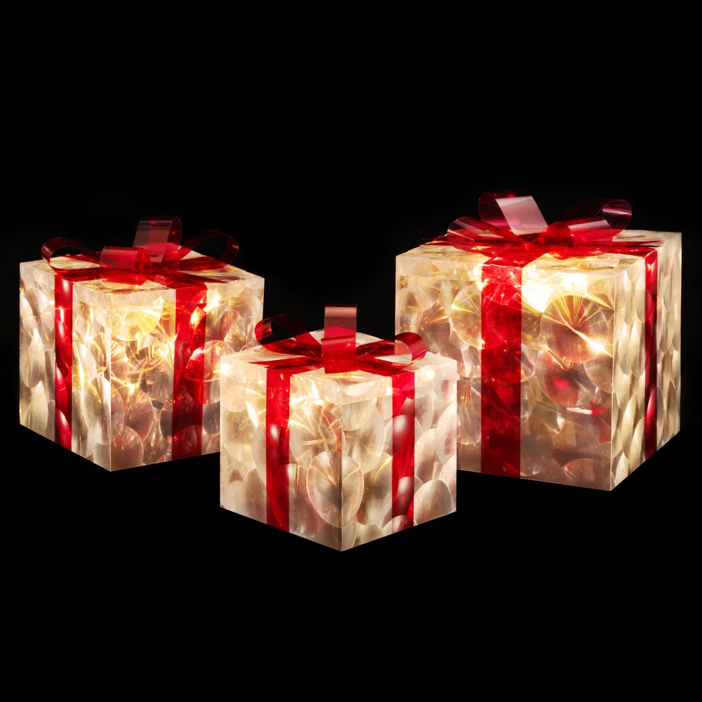 Set of LED fairy lights in clear gift boxes with red ribbon bows, warm glow.