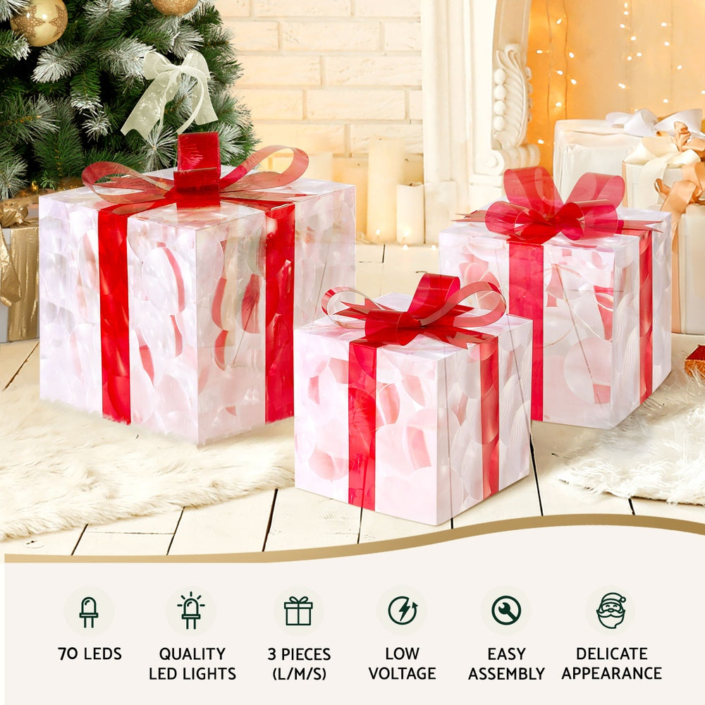 Three illuminated clear gift boxes with red ribbon bows for Christmas decor.