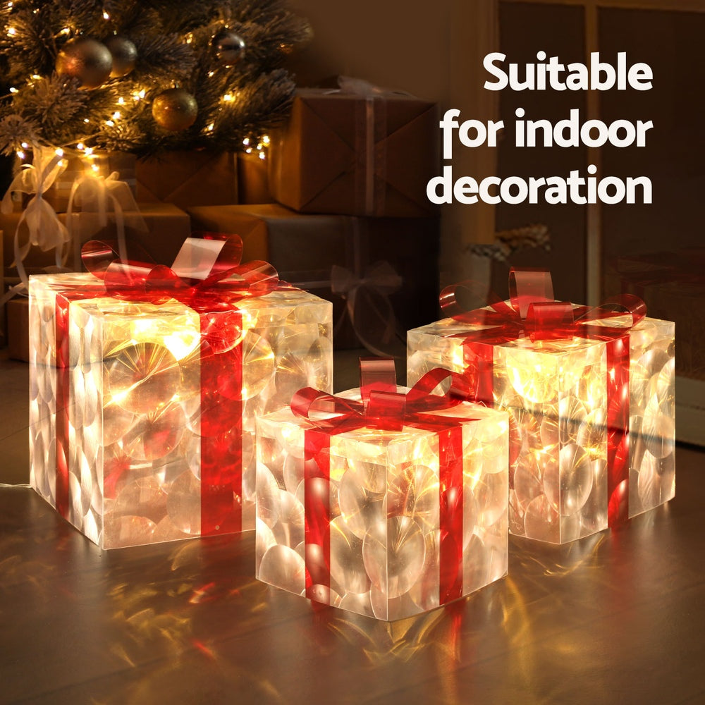 LED lit gift boxes with red ribbon bows and warm light, shown near pine branches.