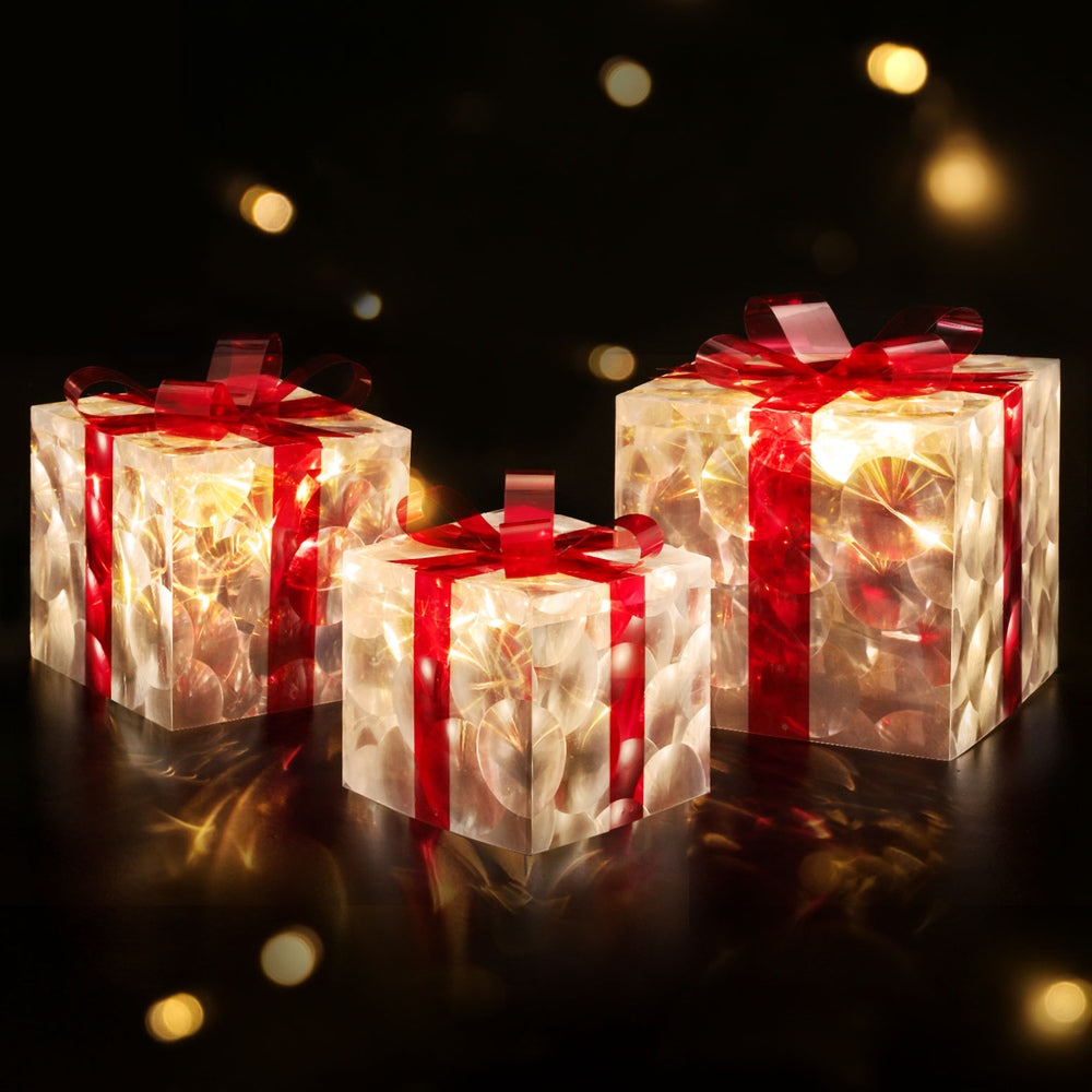 Three warm-glowing LED fairy light gift boxes with red ribbon bows.