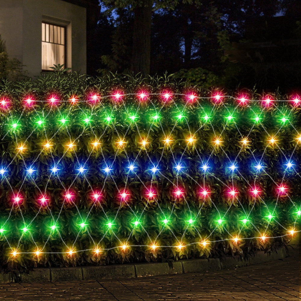 Outdoor hedge wrapped in multicolor LED net string lights with glowing bulbs