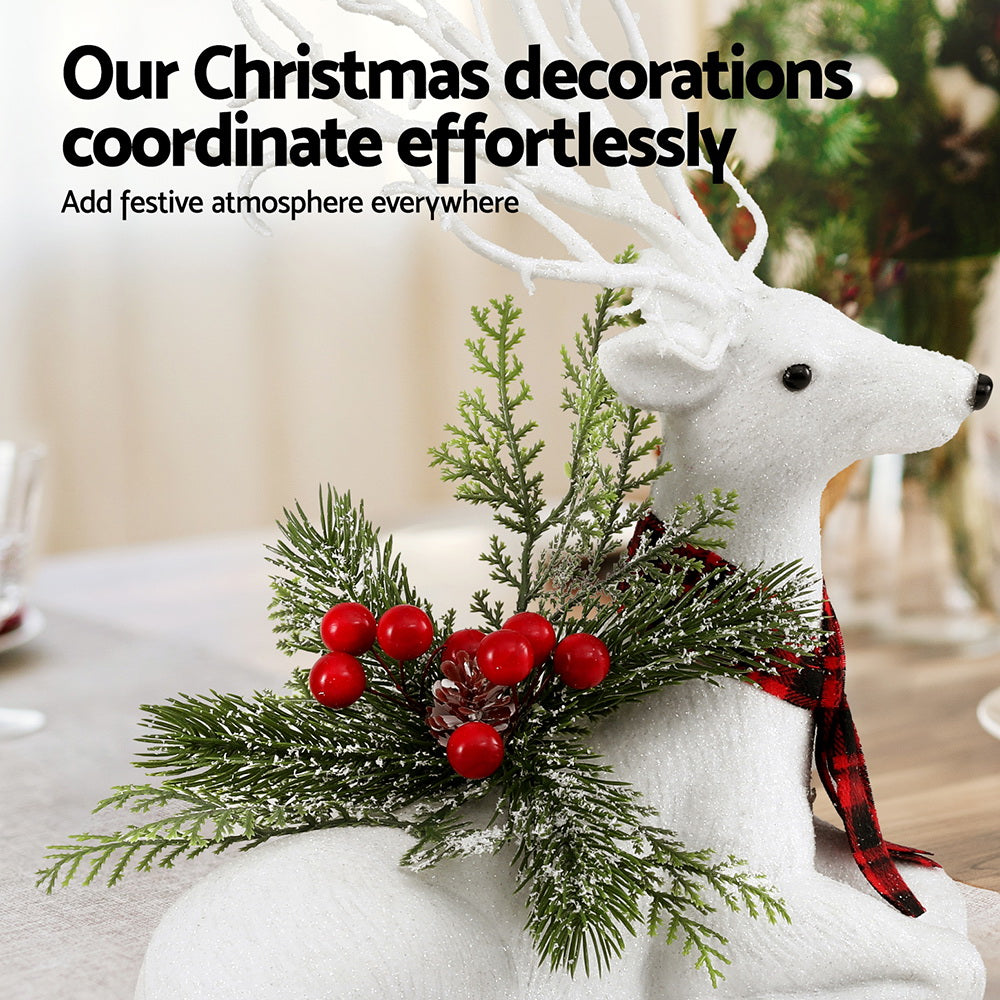 Christmas deer ornament, plush white reindeer with antlers and plaid scarf, surrounded by pine and red berries.